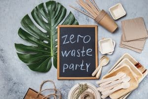 Zero waste party concept. Eco ffriendly tableware, craft bags and monstera leaves on gray background. Top view
