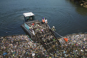 Boat collecting plastic waste from a polluted waterway, highlighting ocean cleanup efforts by Team Seas.