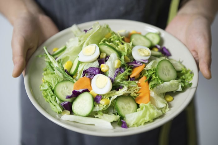 Fresh salad with mixed greens, sliced cucumbers, carrots, corn, and boiled eggs, symbolizing sustainable eating and healthy food choices.