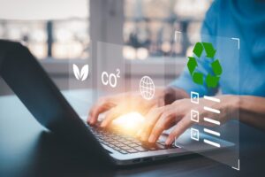 A businessman using a laptop to research something, with recycling, CO2, and leaf symbols floating above the keyboard.