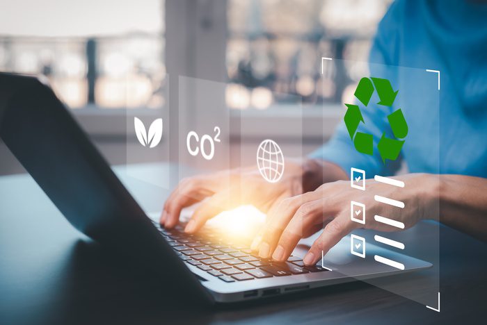 A businessman using a laptop to research something, with recycling, CO2, and leaf symbols floating above the keyboard.