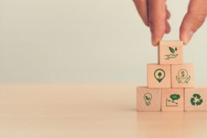 A close-up of a set of wooden blocks on the table. Each block as a green icon painted on. Fingers place the top block.