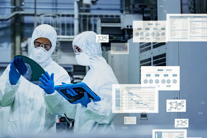 Two cleanroom technicians inspect a silicon wafer and a tablet as digital data panels overlay the image.