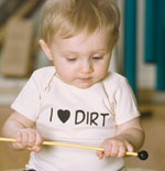 Baby wearing "I ❤️ DIRT" shirt playing with a yellow stick in a playful indoor setting.